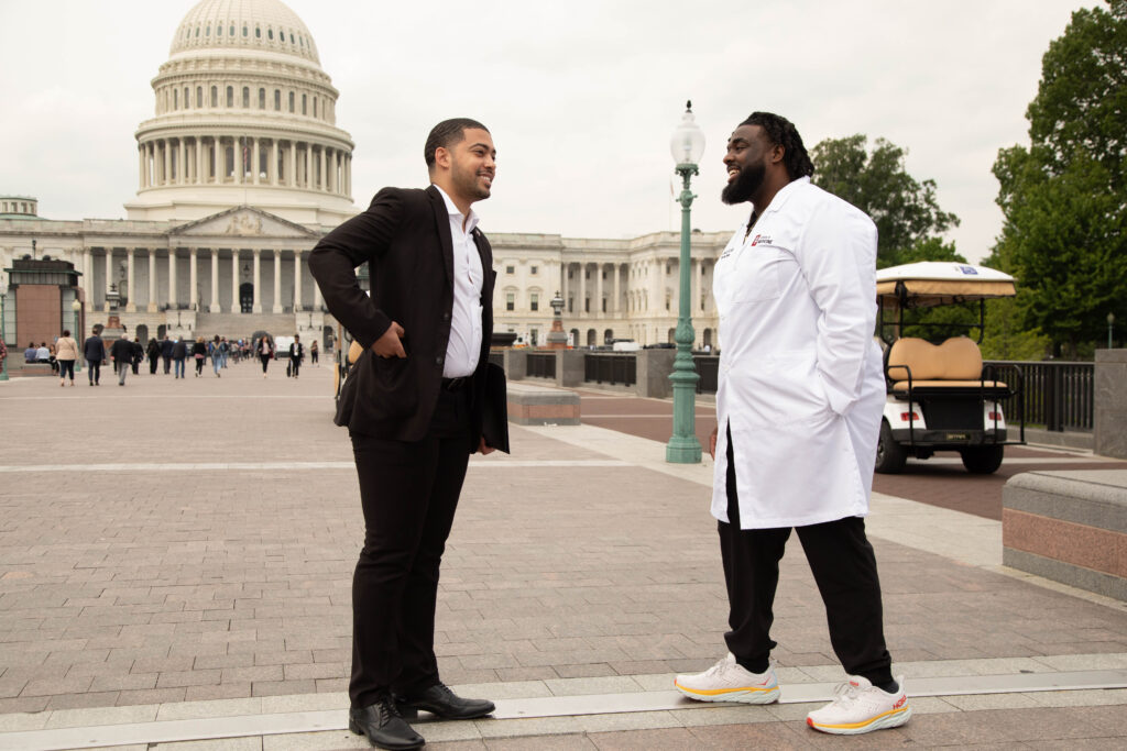 Kylar Wiltz, wearing a suit, and Russell Ledet, MD, wearing a white doctor's coat, stand in front of the U.S. Capitol building before a Congressional Briefing for Black Men and Boys in Medicine